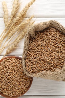 Kase içinde buğday taneleri, çuval bezi torbası ve beyaz ahşap masada çivili kazıklar, düz uzanmış.