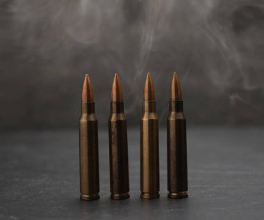 Gri masadaki ateşli silah fişekleri dumana karşı, yakın plan.