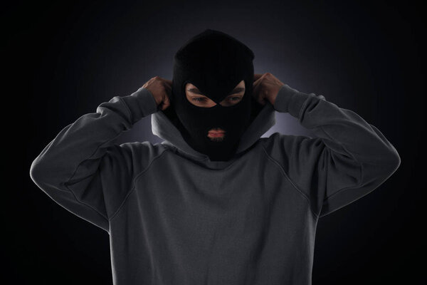 Преступник в маске и капюшоне на темном фоне