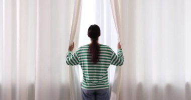 Kadın evde pencere perdelerini açıyor, arka manzara