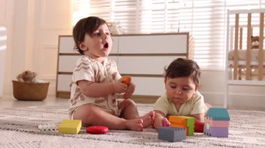 Evde yerde oyuncaklarla oynayan şirin ikiz bebekler.