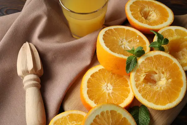 Taze sıkılmış portakal suyu, meyve, nane, meyve sıkacağı ve havluyu ahşap masaya yakın plan.