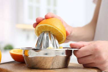 Meyve suyu. İçerideki masada meyve sıkacağı kullanan portakallı kadın, yakın plan.