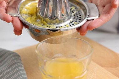 İçerideki masada taze sıkılmış portakal suyunu bardağa dolduran kadın, yakın plan.