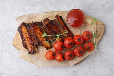 Kızarmış biftek pirzolası, mikroyeşillikler, domatesler ve sosla gri desenli masa, üst manzara.