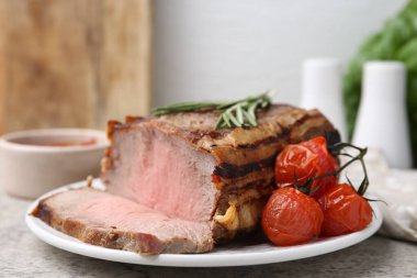 Lezzetli pişmiş et, domates, biberiye ve sos gri masada, yakın plan.