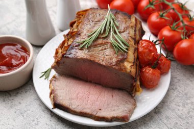 Lezzetli pişmiş et, domates, biberiye ve sos gri masada, yakın plan.