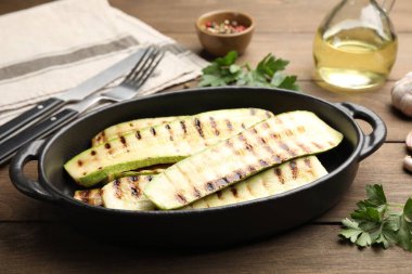 Fırın tabağında lezzetli ızgara kabak dilimleri ve ahşap masada maydanoz, yakın plan.