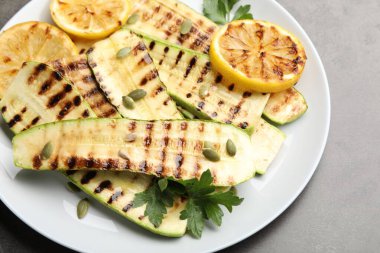 Lezzetli ızgara kabak dilimleri, balkabağı tohumları, limon ve maydanoz, gri masanın üstünde, üst tarafta.