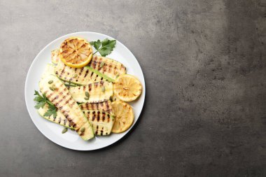 Lezzetli ızgara kabak dilimleri, balkabağı tohumları, limon ve maydanoz, gri desenli masa, üst manzara. Metin için boşluk