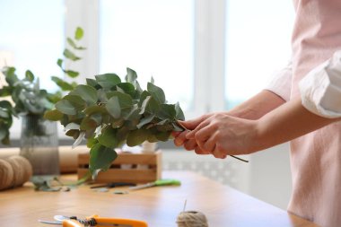 Çiçekçinin ahşap masasında okaliptüs dallarından güzel bir buket yapıyor.