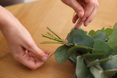 Çiçekçinin ahşap masasında okaliptüs dallarından güzel bir buket yapıyor.