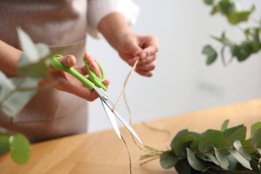 Çiçekçinin ahşap masasında okaliptüs dallarından güzel bir buket yapıyor.