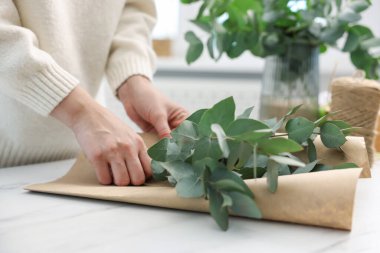 Çiçekçinin beyaz mermer masasında okaliptüs dallarından güzel bir buket yapıyor.