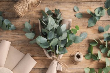 Çiçekçi. Okaliptüs dalları, iplikler ve ambalaj kağıtları ahşap masa üzerinde, düz yatıyordu.