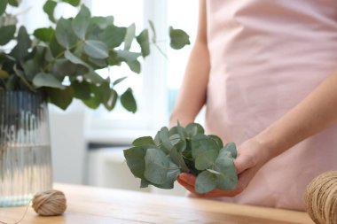 Çiçekçinin ahşap masasında okaliptüs dallarından güzel bir buket yapıyor.