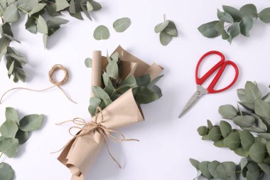 Çiçekçi. Beyaz masa üzerinde okaliptüs dalları, iplik, makas ve ambalaj kağıdı düz.