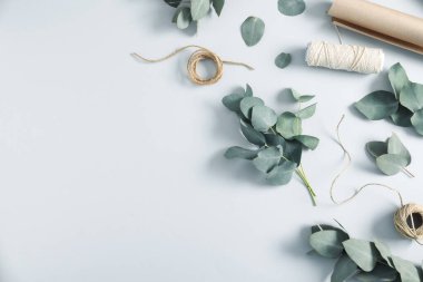 Çiçekçi. Okaliptüs dalları, iplikler ve ambalaj kağıtları beyaz masada, düz yerde. Metin için boşluk
