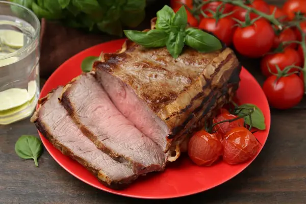 Lezzetli pişmiş et, domates, fesleğen ve ferahlatıcı içecek ahşap masada, yakın plan.