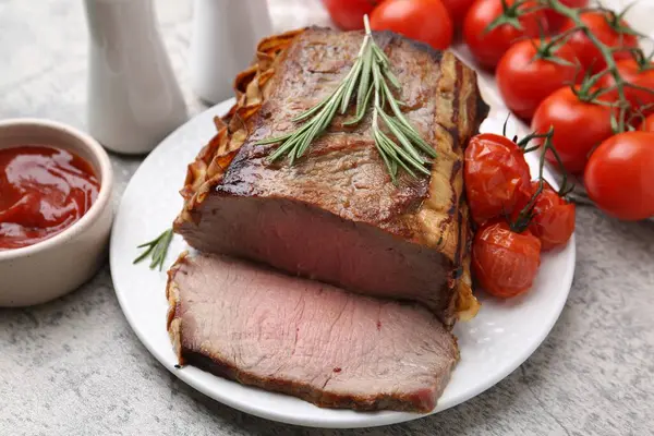 Lezzetli pişmiş et, domates, biberiye ve sos gri masada, yakın plan.