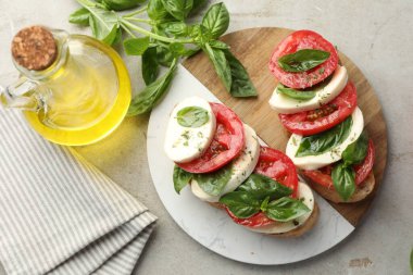 Mozarella peynirli, domatesli ve fesleğenli lezzetli sandviçler gri desenli masa, düz uzanış