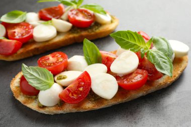 Peynirli, domatesli ve fesleğenli lezzetli sandviçler. Gri desenli masa, yakın plan.