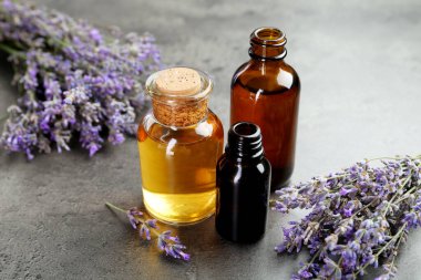 Şişelerdeki yağlar ve gri desenli masadaki lavanta çiçekleri, yakın plan.