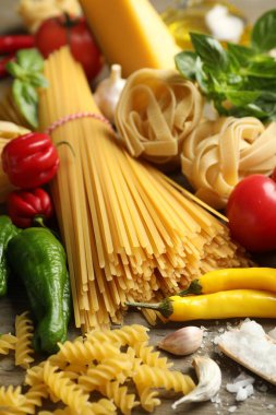 Farklı türde makarna ve malzemeler ahşap masada, yakın plan.
