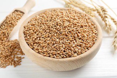 Kasede buğday taneleri, beyaz ahşap masada kepçe ve çiviler, yakın plan.