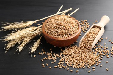 Kâsede buğday taneleri, siyah ahşap masada kepçeler ve çiviler, yakın plan.