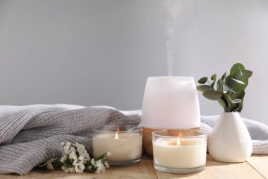 Açık gri arkaplana karşı ahşap masada yanan mumlar ve aroma yağıyla kaplıca kompozisyonu, yakın plan