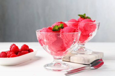 Tatlı kaselerinde naneli ahududu şerbeti, beyaz ahşap masada taze meyveler açık gri arka planda, yakın planda.