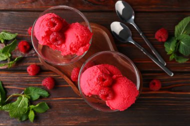 Tatlı kaselerinde nefis ahududu şerbeti, kaşıklar, nane ve taze böğürtlen ahşap masada, düz uzanmış