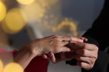 Evlilik teklifi yapıyor. Nişan yüzüğünü evde kız arkadaşının parmağına takan bir adam, yakın plan. Bokeh etkisi