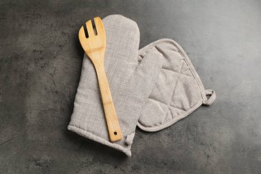 Gri fırın eldiveni, tutkal ve koyu dokulu masa üzerinde ahşap salata sunucusu.