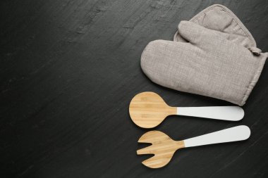 Gri fırın eldiveni ve diğer mutfak gereçleri koyu dokulu masada, düz yerde. Metin için boşluk