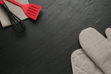 Gri fırın eldiveni ve diğer mutfak gereçleri koyu dokulu masada, düz yerde. Metin için boşluk