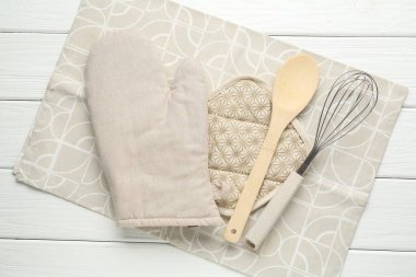 Fırın eldiveni ve diğer mutfak gereçleri beyaz ahşap masada, üst tarafta.