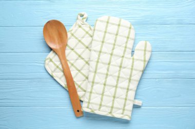 Fırın eldiveni, tutucu ve kaşık açık mavi ahşap arka planda, düz yatıyordu.