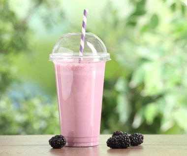 Plastik bardaktaki lezzetli milkshake ve dışarıdaki ahşap masada böğürtlen.