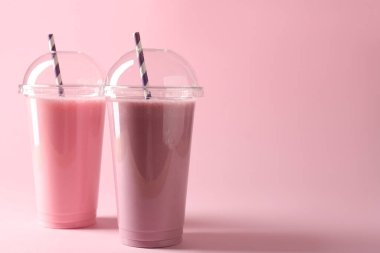 Pembe arka planda plastik bardaklarda lezzetli milkshake 'ler, metin için boşluk