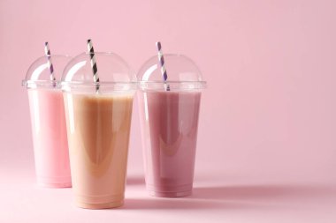 Pembe arka planda plastik bardaklarda lezzetli milkshake 'ler, metin için boşluk