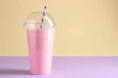 Renkli arka planda plastik bardakta lezzetli milkshake, metin için boşluk