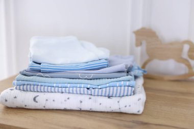 Beyaz duvarın yakınındaki ahşap masada temiz bebek kıyafetleri yığını.