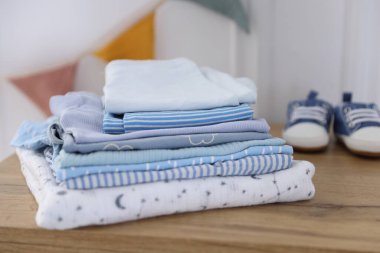 İçerideki ahşap masada temiz bebek kıyafetleri ve ayakkabılar yığını.