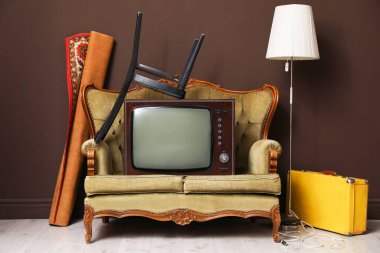 Kanepe, sandalye, bavul, lamba ve halı kahverengi duvarın yanında. Kullanılmış eşyalar