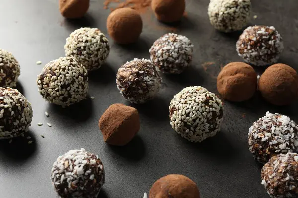 Gri masada kakao tozu, fındık, hindistan cevizi gevreği ve susam tohumlu lezzetli çikolata şekerleri, yakın plan.