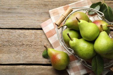 Metal sepetin içinde taze armutlar ve ahşap masanın üzerinde yeşil yapraklar. Metin için boşluk