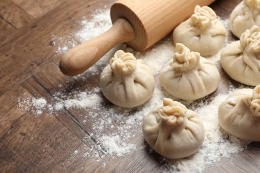 Ahşap masa üzerinde merdane ve un ile pişirilmemiş khinkaliler (hamur tatlısı), yakın plan