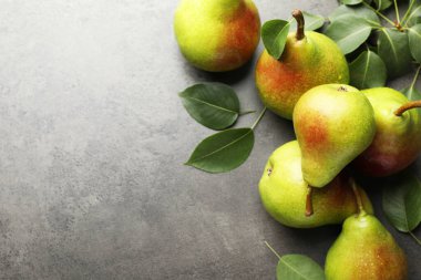 Taze armutlar ve yeşil yapraklar gri masada, düz yerde. Metin için boşluk